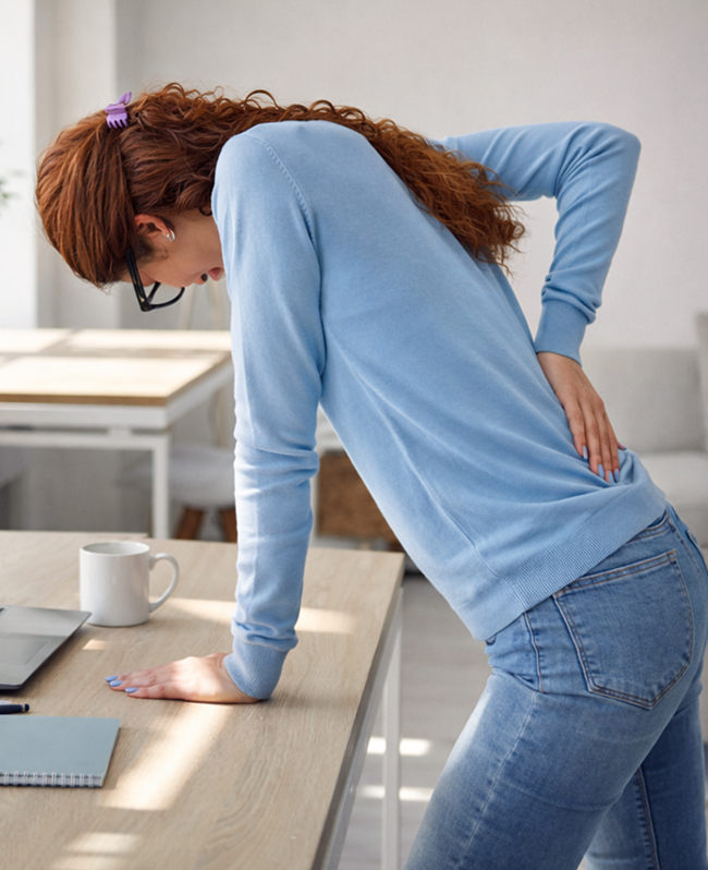 Woman experiencing lower back pain while leaning on a desk